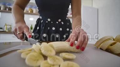 女人在家庭厨房的木制厨房板上切香蕉。 在家做饭。 厨房里的家庭气氛